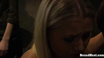 in the dungeon, a mistress whips and humiliates her bound submissive teen companion
