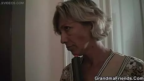 A middle aged blonde woman sucking two young men’s cocks